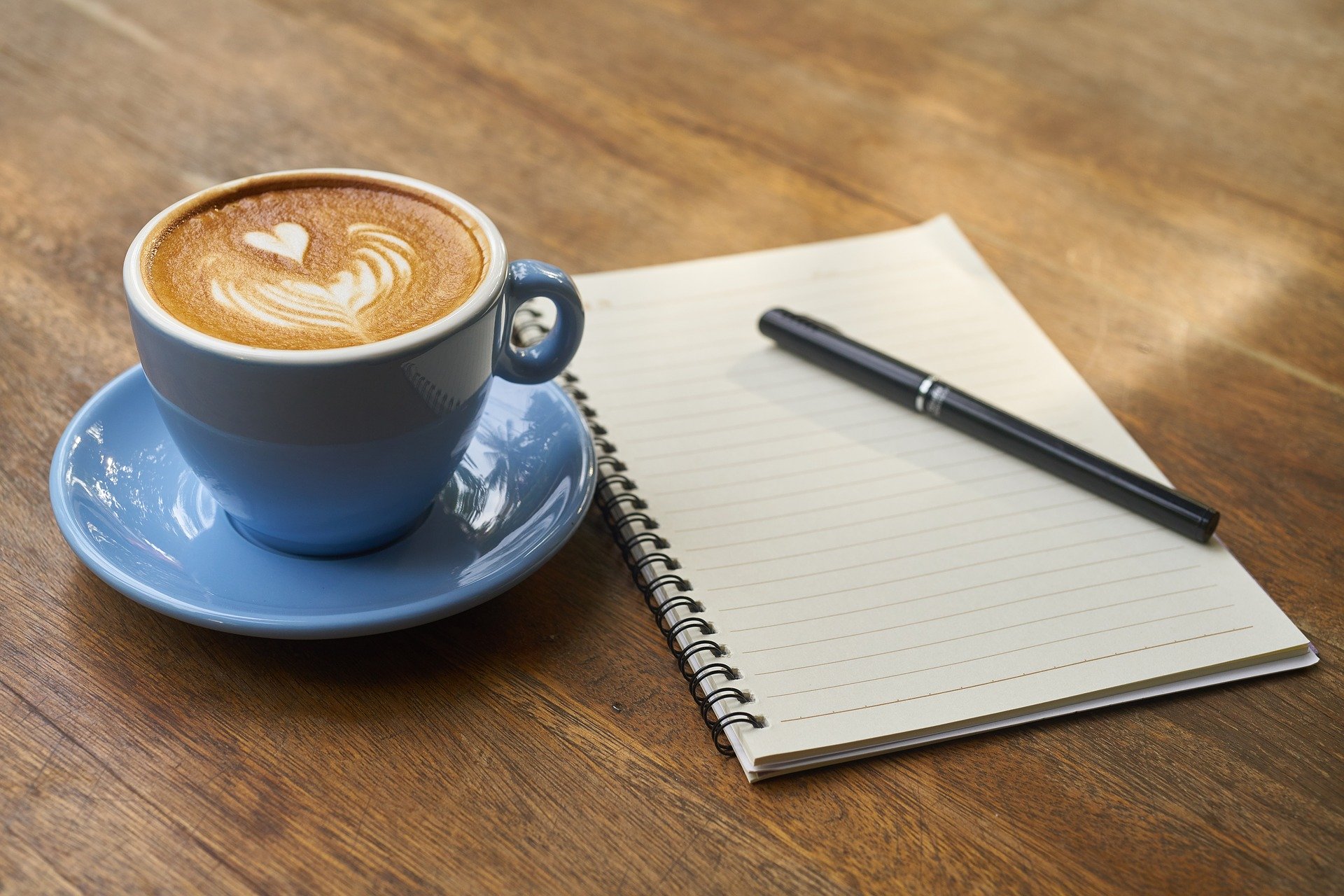 Ein Holztisch mit einer Tasse Kaffee und einem Schreibblock mit Stift.